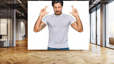 Young hispanic man wearing casual white t shirt gesturing finger crossed smiling with hope and eyes closed. luck and superstitious concept. Wall mural