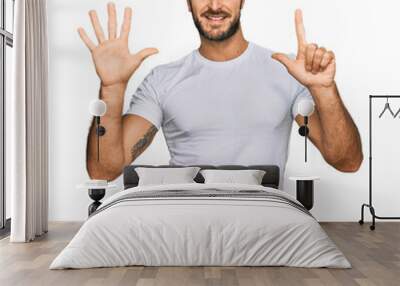 Young hispanic man wearing casual white t shirt showing and pointing up with fingers number seven while smiling confident and happy. Wall mural