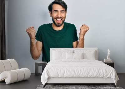 Young hispanic man wearing casual white tshirt celebrating surprised and amazed for success with arms raised and open eyes. winner concept. Wall mural