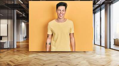 Young hispanic man wearing casual yellow t shirt sticking tongue out happy with funny expression. emotion concept. Wall mural