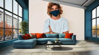 Young hispanic man wearing covid-19 mask happy face smiling with crossed arms looking at the camera. positive person. Wall mural