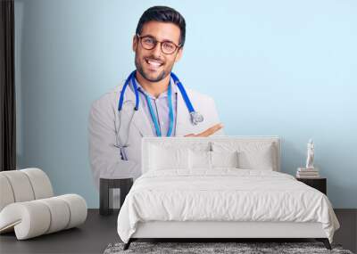 Young hispanic man wearing doctor uniform and stethoscope cheerful with a smile on face pointing with hand and finger up to the side with happy and natural expression Wall mural