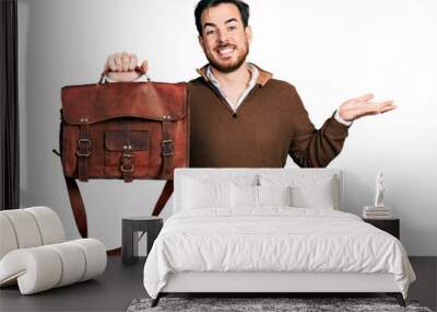 Young hispanic man wearing leather bag celebrating achievement with happy smile and winner expression with raised hand Wall mural