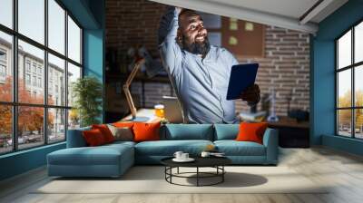 Young hispanic man with beard and tattoos working at the office at night smiling confident touching hair with hand up gesture, posing attractive and fashionable Wall mural