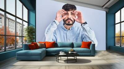 Young hispanic man with beard standing over blue background trying to open eyes with fingers, sleepy and tired for morning fatigue Wall mural