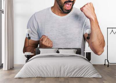 Young hispanic man with beard wearing casual grey t shirt celebrating surprised and amazed for success with arms raised and eyes closed Wall mural