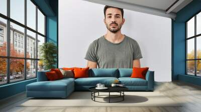 Young hispanic man with beard wearing casual t shirt over white background relaxed with serious expression on face. simple and natural looking at the camera. Wall mural