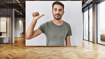 Young hispanic man with beard wearing casual t shirt over white background showing and pointing up with finger number one while smiling confident and happy. Wall mural