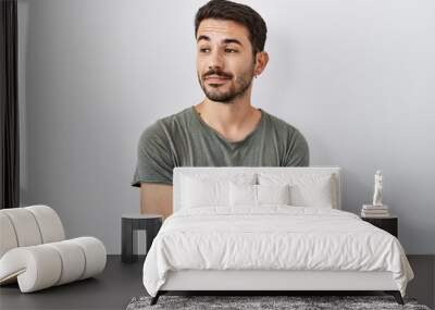 Young hispanic man with beard wearing casual t shirt over white background smiling looking to the side and staring away thinking. Wall mural