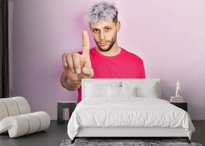 Young hispanic man with modern dyed hair wearing casual pink t shirt pointing with finger up and angry expression, showing no gesture Wall mural