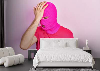 Young hispanic man with modern dyed hair wearing pink balaclava mask face surprised with hand on head for mistake, remember error. forgot, bad memory concept. Wall mural