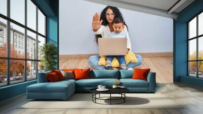 Young hispanic mother and kid using computer laptop sitting on the floor doing stop sing with palm of the hand. warning expression with negative and serious gesture on the face. Wall mural