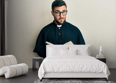 Young hispanic priest man holding bible skeptic and nervous, frowning upset because of problem. negative person. Wall mural