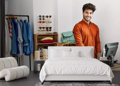 Young hispanic shopkeeper man smiling happy working at clothing store. Wall mural