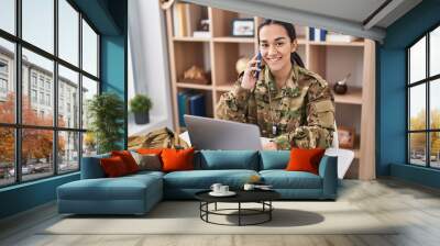 Young hispanic woman army soldier using laptop and talking on martphone at home Wall mural