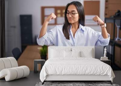 Young hispanic woman at the office showing arms muscles smiling proud. fitness concept. Wall mural