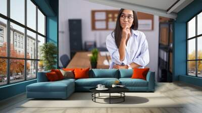 Young hispanic woman at the office with hand on chin thinking about question, pensive expression. smiling with thoughtful face. doubt concept. Wall mural