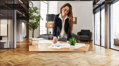 Young hispanic woman business worker writing on paperwork working at office Wall mural