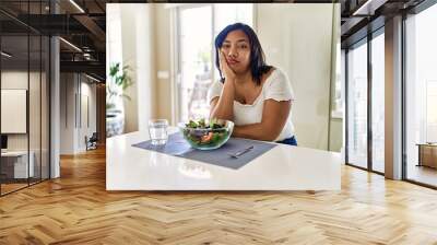 Young hispanic woman eating healthy salad at home thinking looking tired and bored with depression problems with crossed arms. Wall mural