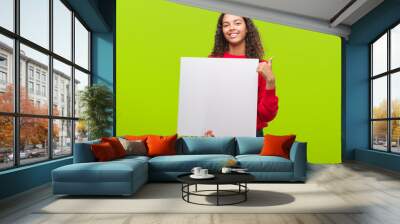 Young hispanic woman holding blank banner happy with big smile doing ok sign, thumb up with fingers, excellent sign Wall mural