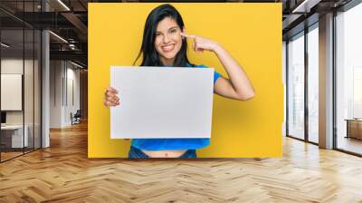 Young hispanic woman holding blank empty banner pointing finger to one self smiling happy and proud Wall mural