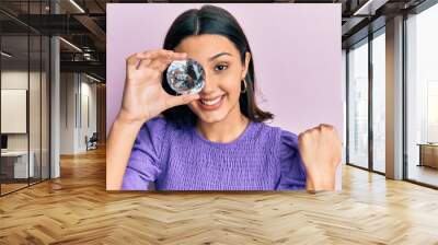 Young hispanic woman holding brilliant diamond stone pointing thumb up to the side smiling happy with open mouth Wall mural