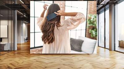 Young hispanic woman on back view combing hair at home Wall mural