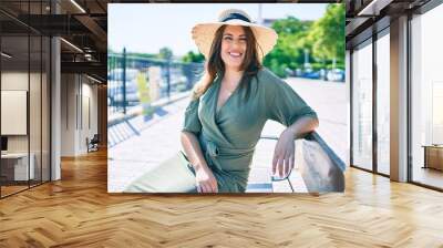 Young hispanic woman on vacation smiling happy sitting on bench at street of city Wall mural