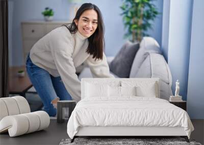 Young hispanic woman organizing sofa at home Wall mural