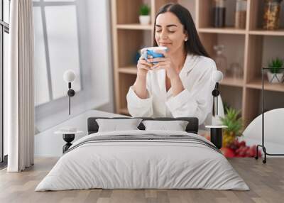 Young hispanic woman reading book drinking coffee at home Wall mural