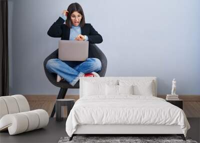 Young hispanic woman sitting on chair using computer laptop looking at the watch time worried, afraid of getting late Wall mural