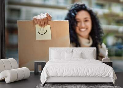 Young hispanic woman smiling confident holding take away paper bag at street Wall mural