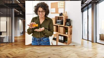 Young hispanic woman smiling confident taking pills at office Wall mural