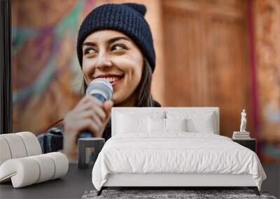 Young hispanic woman smiling happy using headphones and microphone at the city. Wall mural