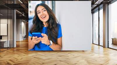 Young hispanic woman smiling happy using smartphone at the city. Wall mural