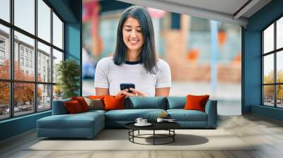 Young hispanic woman smiling happy using smartphone at the city. Wall mural