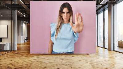 Young hispanic woman standing over pink background doing stop sing with palm of the hand. warning expression with negative and serious gesture on the face. Wall mural