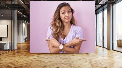 Young hispanic woman standing over pink background pointing to both sides with fingers, different direction disagree Wall mural