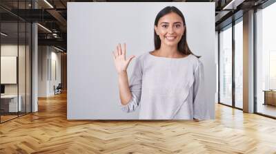 Young hispanic woman standing over white background showing and pointing up with fingers number five while smiling confident and happy. Wall mural