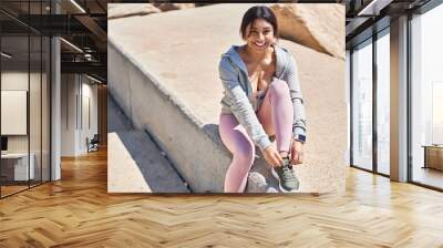 Young hispanic woman tying shoe sitting on floor at street Wall mural