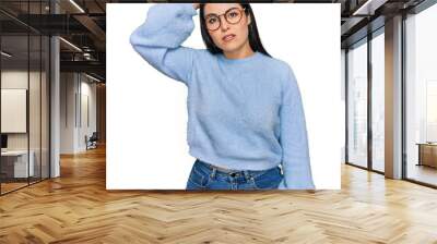 Young hispanic woman wearing casual clothes and glasses confuse and wonder about question. uncertain with doubt, thinking with hand on head. pensive concept. Wall mural