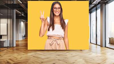 Young hispanic woman wearing casual clothes and glasses showing and pointing up with fingers number two while smiling confident and happy. Wall mural