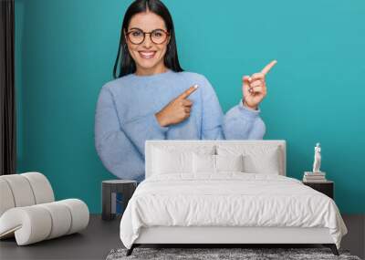 Young hispanic woman wearing casual clothes and glasses smiling and looking at the camera pointing with two hands and fingers to the side. Wall mural