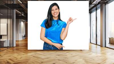 Young hispanic woman wearing casual clothes with a big smile on face, pointing with hand and finger to the side looking at the camera. Wall mural