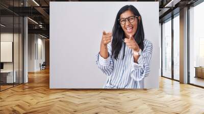 Young hispanic woman wearing glasses pointing fingers to camera with happy and funny face. good energy and vibes. Wall mural