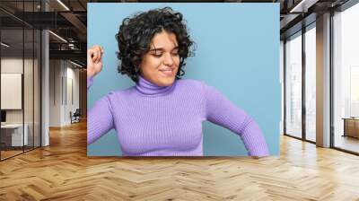 Young hispanic woman with curly hair wearing casual clothes dancing happy and cheerful, smiling moving casual and confident listening to music Wall mural