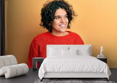 Young hispanic woman with curly hair wearing casual winter sweater looking away to side with smile on face, natural expression. laughing confident. Wall mural