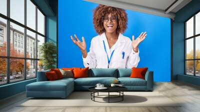 Young hispanic woman with curly hair wearing white coat and id card celebrating victory with happy smile and winner expression with raised hands Wall mural