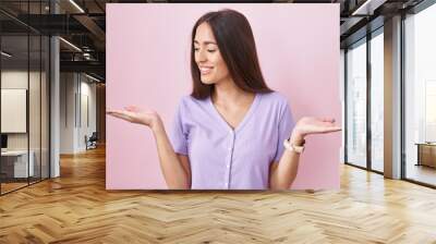 Young hispanic woman with long hair standing over pink background smiling showing both hands open palms, presenting and advertising comparison and balance Wall mural