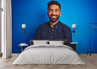 Young indian elegant man wearing shirt standing over isolated blue background happy face smiling with crossed arms looking at the camera. Positive person. Wall mural